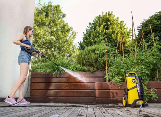 photo of a woman spraying a wooden deck with a power washer