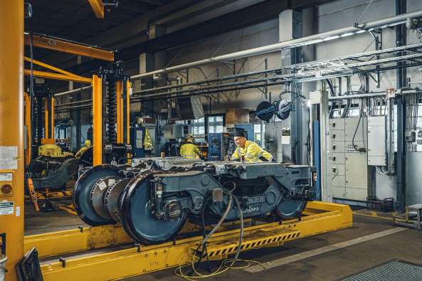 photo of the inside of a rail maintenance plant with people working in yellow safety gear