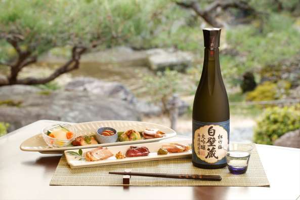 product photo of a sake bottle and sushi placed outside next to a river