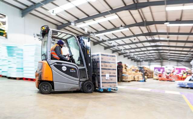 photo of a man driving a forklift with materials through a warehouse