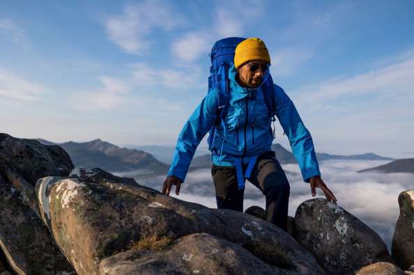 photo of a man with climbing gear climbing up a large mountain