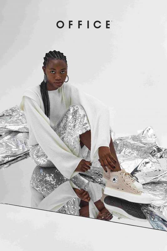 photo of woman posing on a mirror wearing converse and silver clothing for an office photoshoot