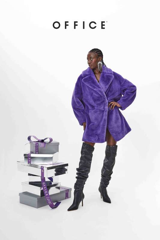 photo of a model wearing a large purple coat and long black boots in a fashion shoot