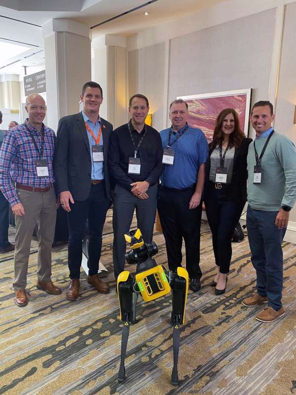 group of infor employees posing in front of a robot prototype at an industry event